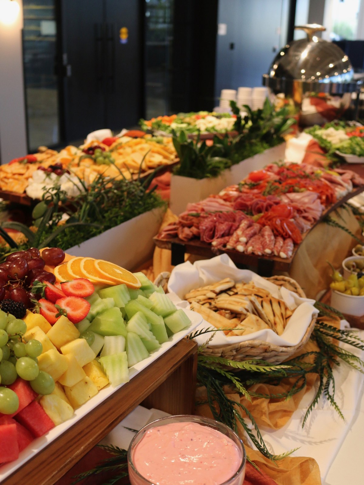 Buffet line of sliced melon and grapes, cured meats, cheeses and crostini running the length of a linen-draped table