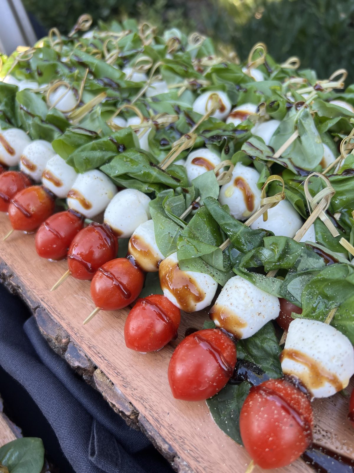 Caprese skewers of cherry tomato, fresh mozzarella and basil drizzled with balsamic glaze on a wooden board