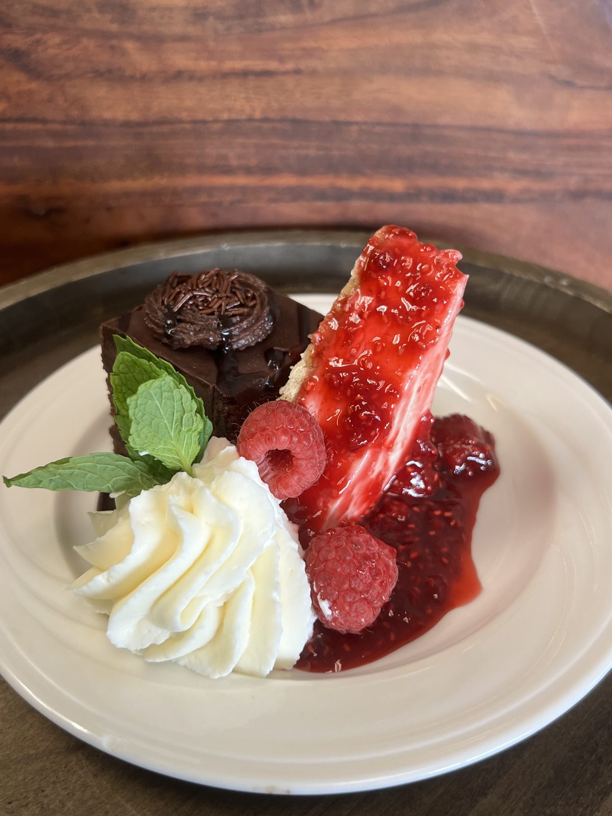 Plated dessert of strawberry cheesecake and chocolate torte with whipped cream, raspberries and mint