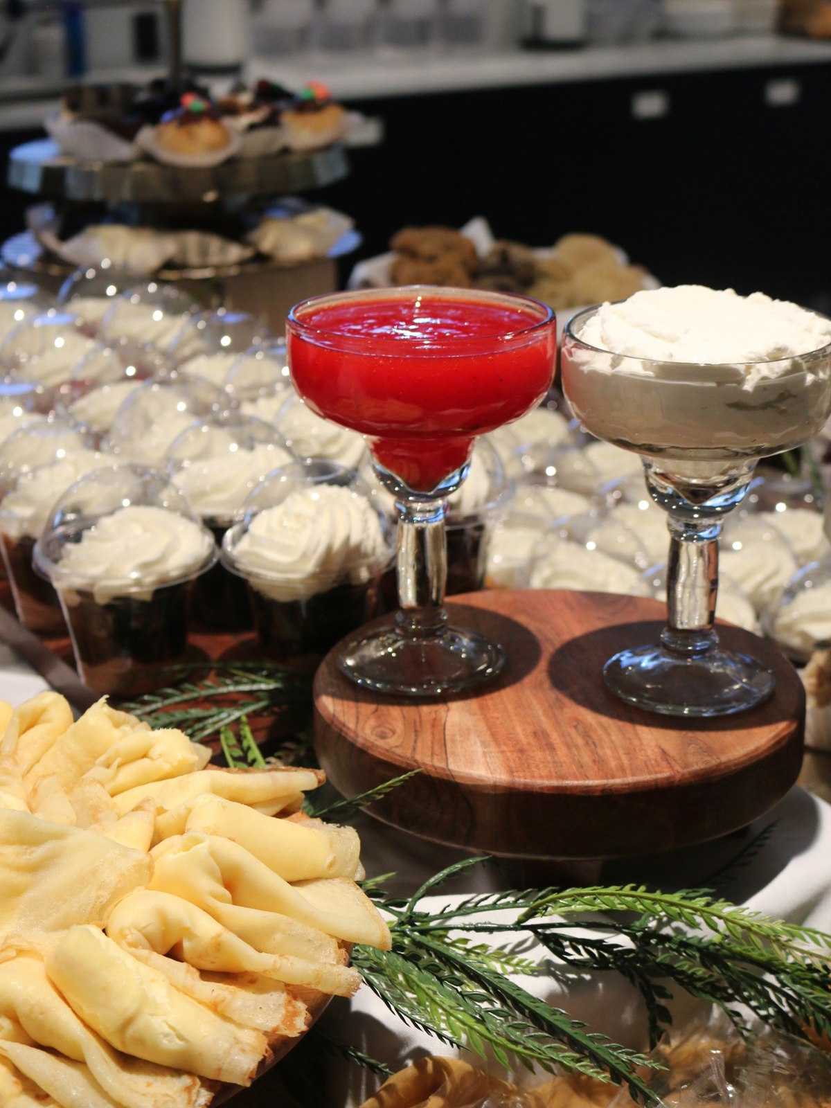 Dessert display of whipped-cream mousse cups with strawberry and cream parfaits served in margarita glasses on a walnut riser