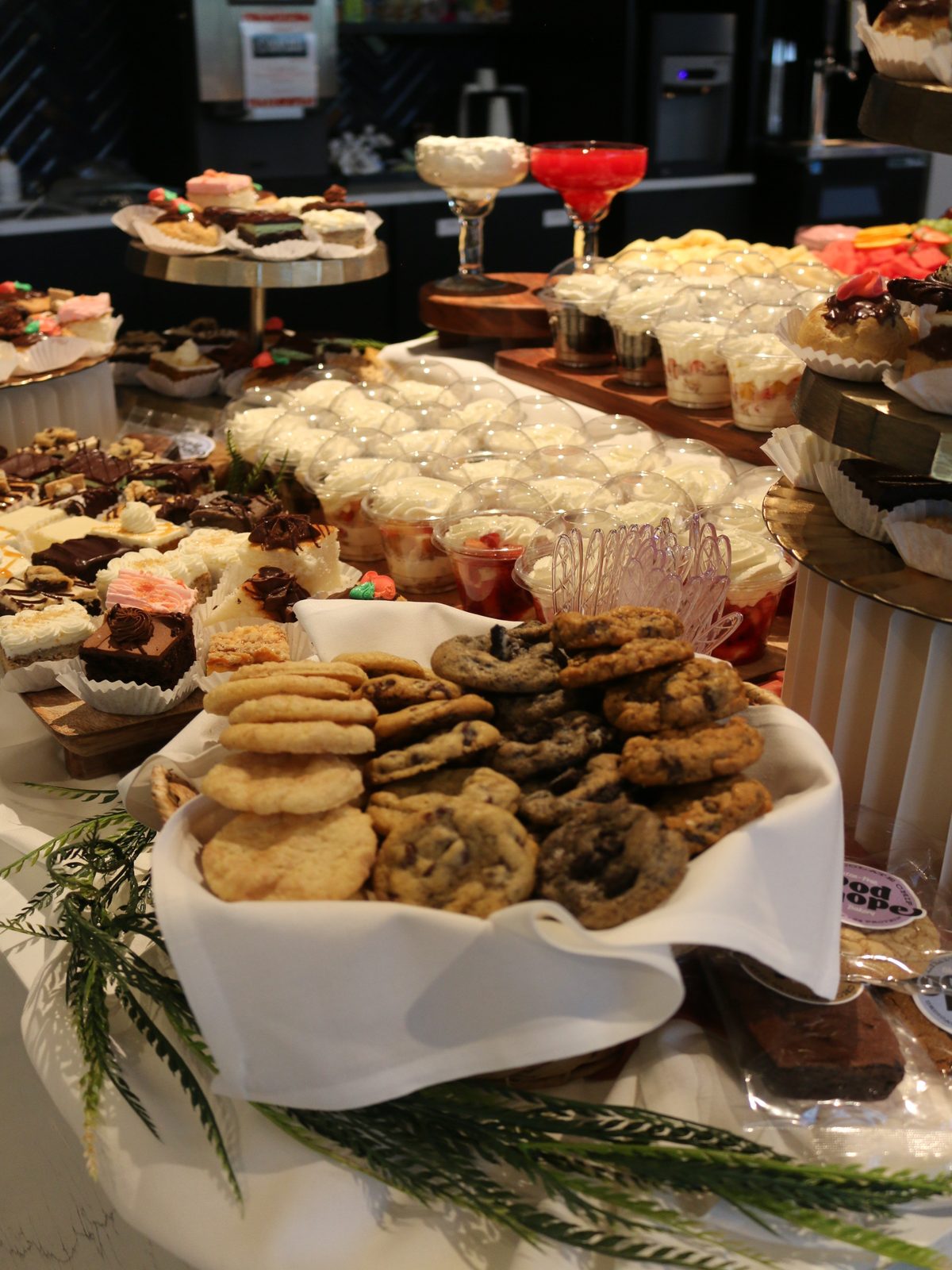 Dessert table of cookies, brownies, cheesecake bars, whipped-cream cups and cupcakes arranged on tiered wooden stands