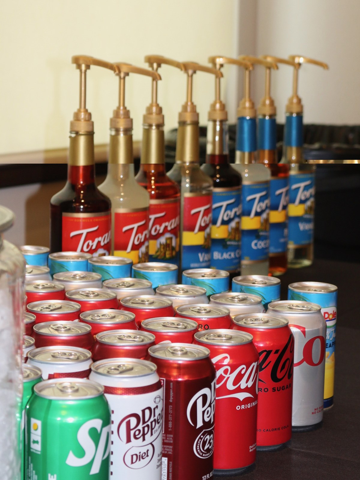 Beverage station with flavoured syrup pumps lined up behind rows of chilled soda cans
