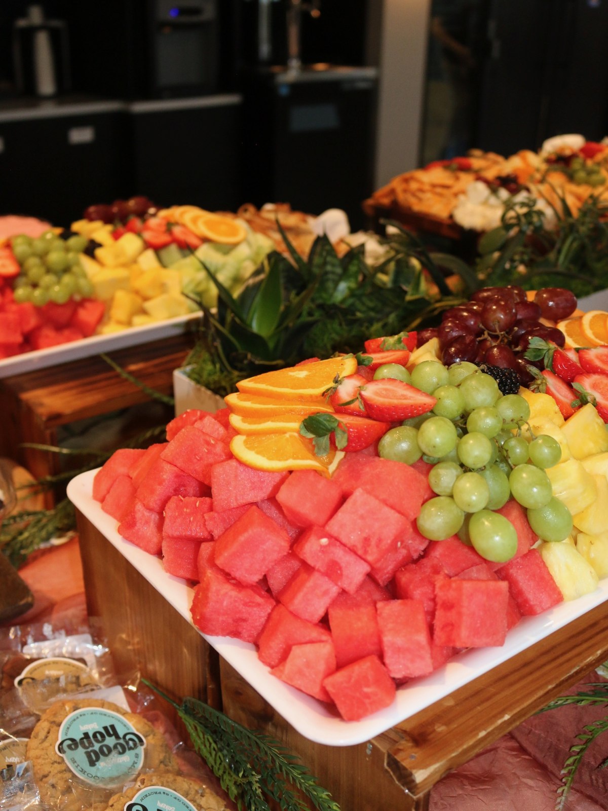 Fresh fruit display of cubed watermelon, orange slices, green grapes and pineapple arranged on tiered wooden risers
