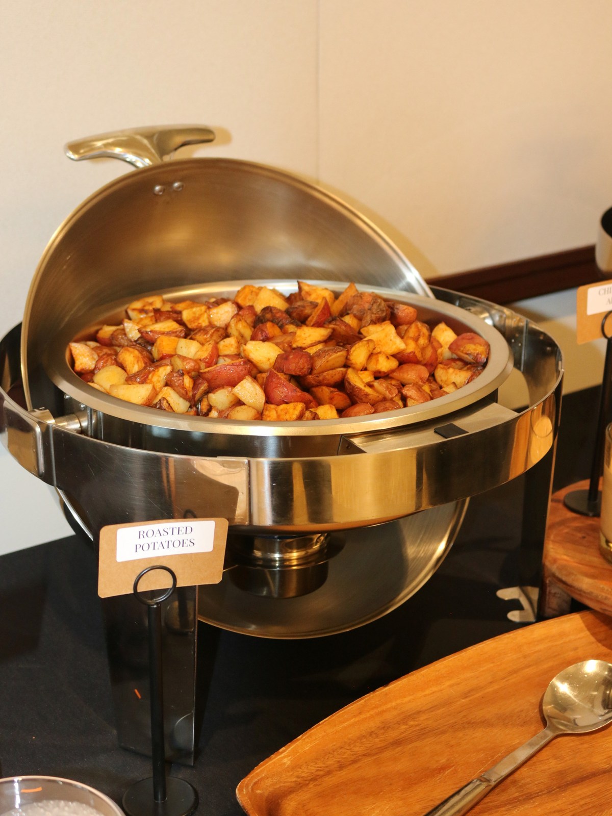 Roll-top chafing dish of herb-roasted red potatoes on a black-linen buffet, labelled for service