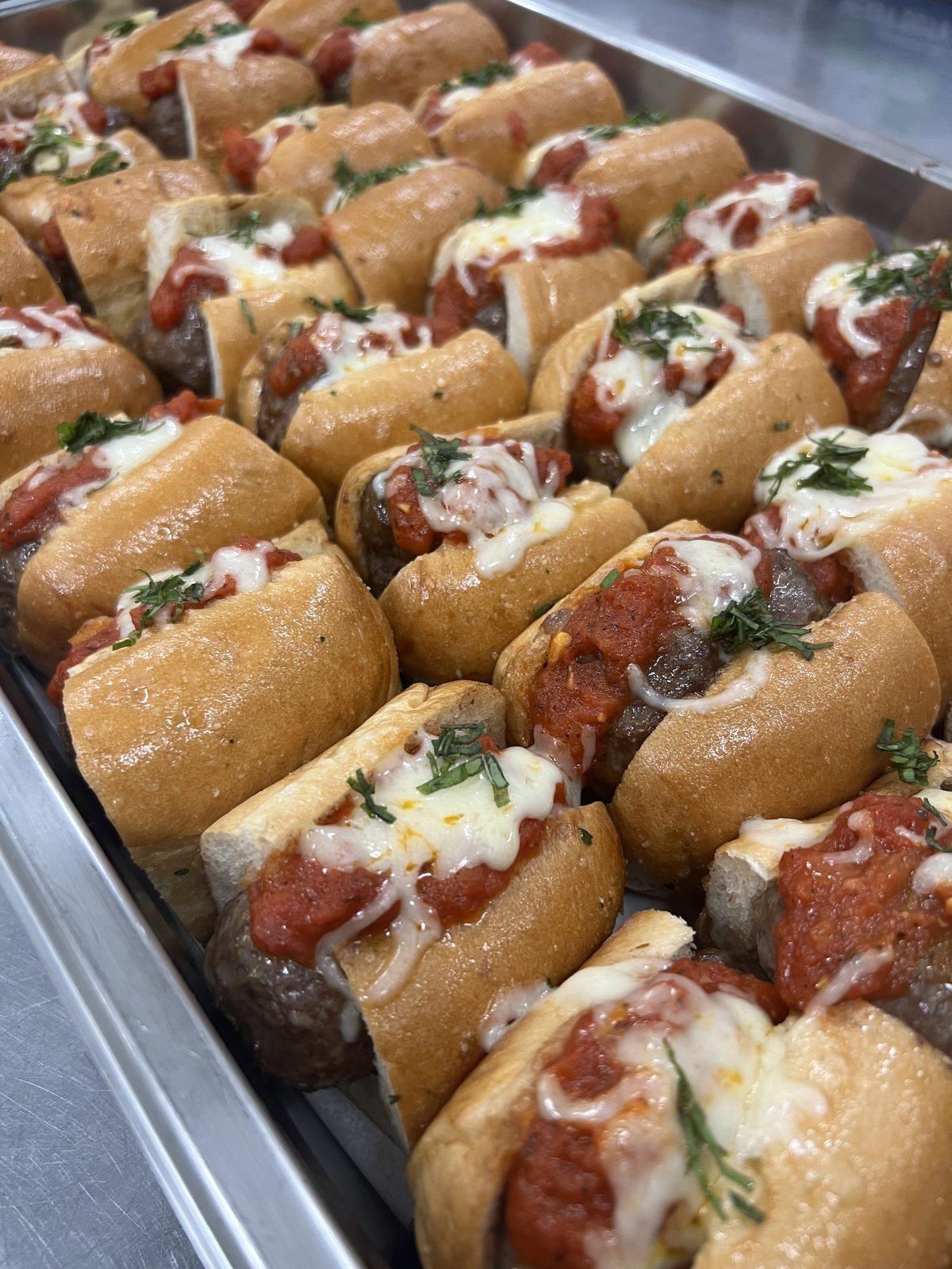 Tray of meatball sliders on toasted rolls with marinara and melted mozzarella, finished with fresh basil